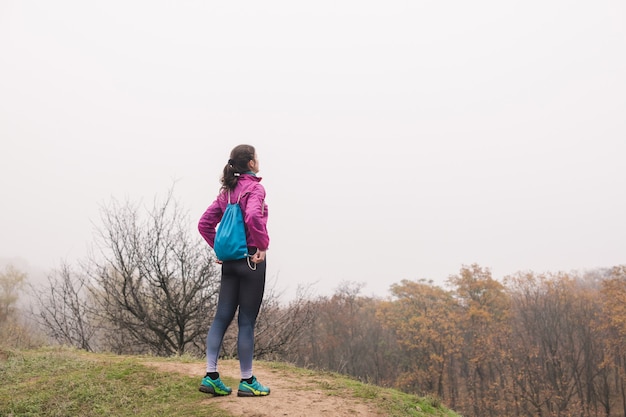 Belle jeune femme sportive en forme saine avec petit sac à dos sur fond de forêt brumeuse