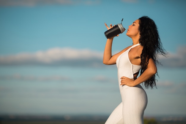 belle jeune femme en survêtement blanc en été avec shaker