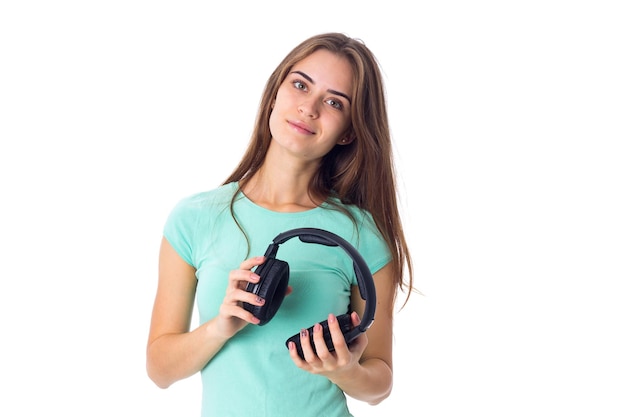 Belle jeune femme en T-shirt bleu tenant un casque noir sur fond blanc en studio