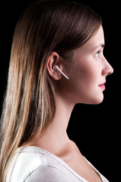 Photo belle jeune femme avec des taches de rousseur et des écouteurs sans fil sur ses oreilles. tourné en studio sur fond noir..