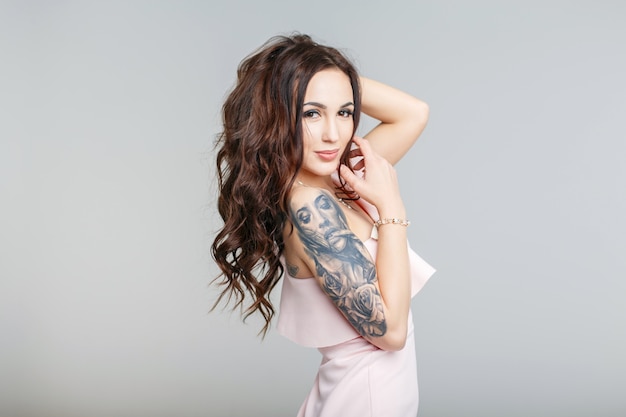 Belle jeune femme avec un tatouage élégant sur place en robe rose sur fond gris