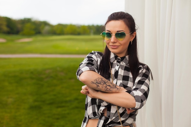 La belle jeune femme avec le tatouage se tient près d'un rideau blanc sur le fond de la nature