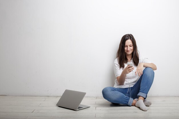 Belle jeune femme avec téléphone portable et écouteurs écoutant de la musique à côté de son ordinateur portable ouvert