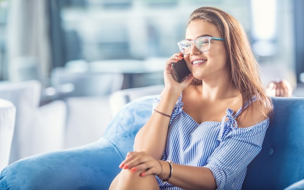 Belle jeune femme avec téléphone portable à la maison ou dans un café.