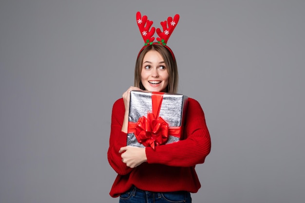 Belle jeune femme tenant une boîte-cadeau en cornes rouges sur un mur gris