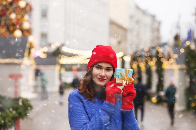 Belle jeune femme tenant une boîte-cadeau avec un ruban à la foire de Noël. Espace libre