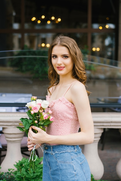 Une belle jeune femme tenant un bouquet de roses et debout près des balustres de la ville et souriant