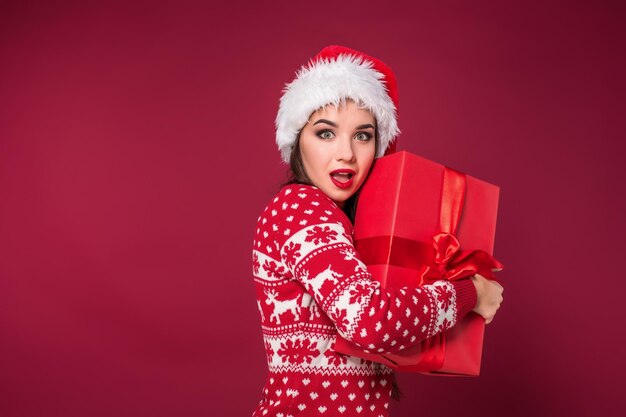 Belle jeune femme tenant un cadeau de Noël dans ses mains sur fond de studio rouge