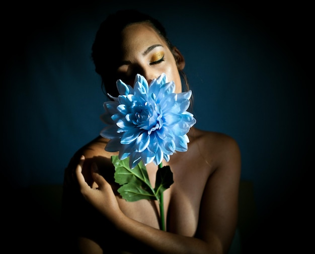 Photo une belle jeune femme tenant une fleur sur un fond bleu