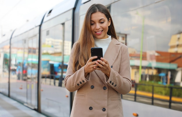 Belle jeune femme tenant des informations de mise à jour cellulaire sur les transports urbains en ligne. Femme d'affaires souriante satisfaite du service de billetterie en ligne payant le transport électrique via smartphone.