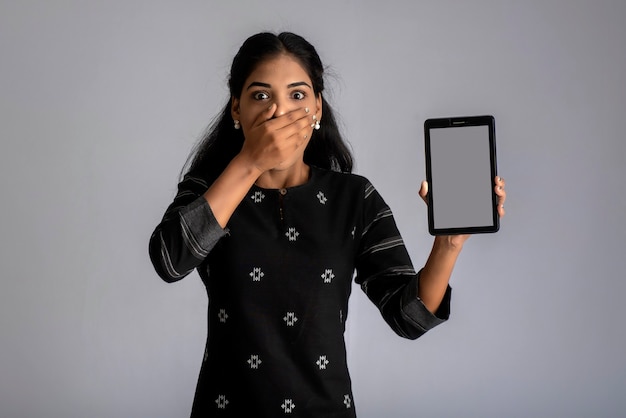 Belle jeune femme tenant et montrant un écran vide de téléphone intelligent ou mobile ou tablette sur un gris.