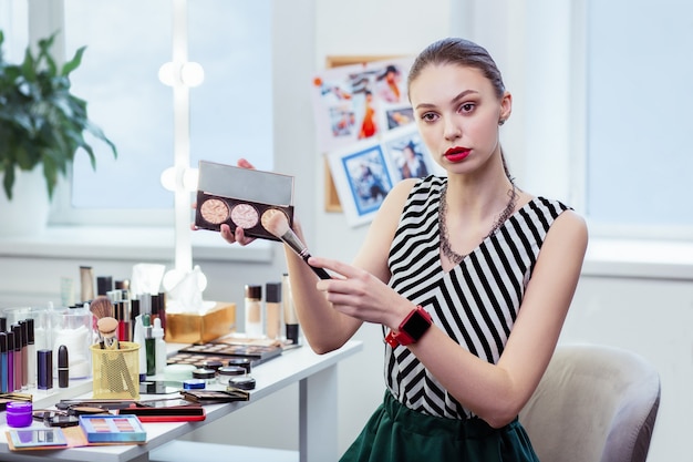 Belle jeune femme tenant une palette de poudre lors de l'application sur le pinceau