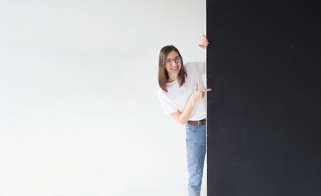 Une belle jeune femme tenant un panneau d'affichage vide pointe son doigt vers un isolé sur un blanc