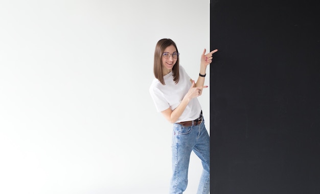 Une belle jeune femme tenant un panneau d'affichage vide pointe son doigt vers un isolé