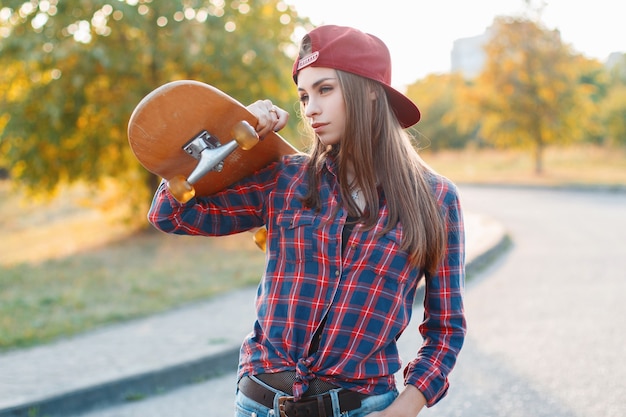 Belle jeune femme tenant une planche à roulettes dans le parc au coucher du soleil