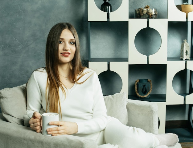 Belle jeune femme tenant une tasse de café et assis sur une chaise à la maison Concept de style de vie et de personnes
