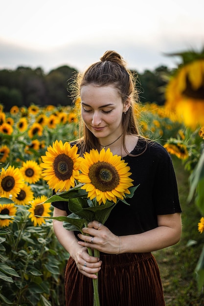Une belle jeune femme tenant des tournesols alors qu'elle se tient à la ferme