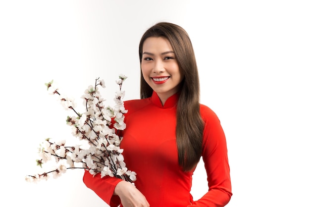 Belle jeune femme en tenue asiatique (ao dai), tenant une fleur, regardant la caméra, souriant.