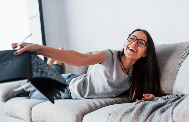 Belle jeune femme en tenue décontractée allongée seule à la maison avec un bloc-notes et un stylo.