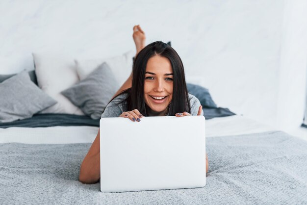 Belle jeune femme en tenue décontractée allongée seule à la maison avec un ordinateur portable.