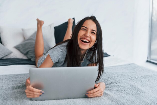 Belle jeune femme en tenue décontractée allongée seule à la maison avec un ordinateur portable.