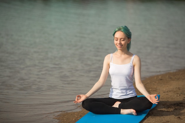 Belle jeune femme en tenue de sport, faire du yoga près du lac