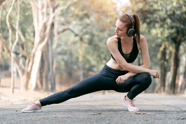 Belle jeune femme en tenue de sport faisant des étirements avant l'entraînement en plein air dans le parc pour avoir un mode de vie sain