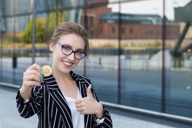 La belle jeune femme tient le bitcoin dans une main. Elle est une femme d'affaires et a investi son argent dans la crypto-monnaie, prévoyant de gagner beaucoup d'argent dessus.