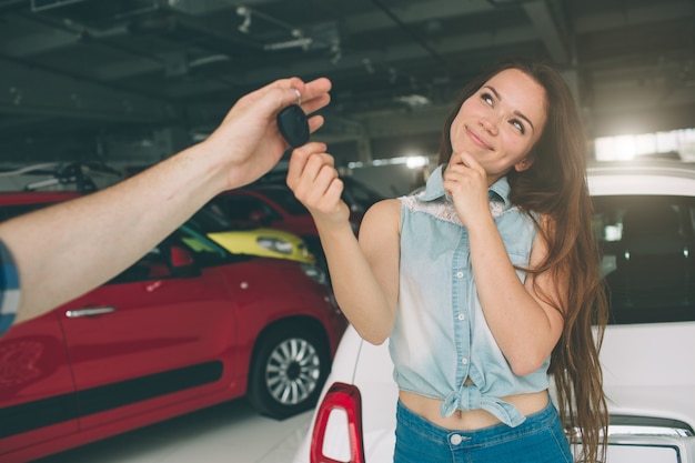 Belle jeune femme tient une clé dans le concessionnaire automobile