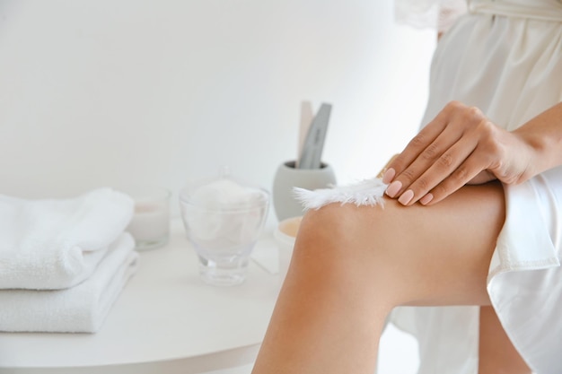 Belle jeune femme touchant la jambe avec une plume à la maison