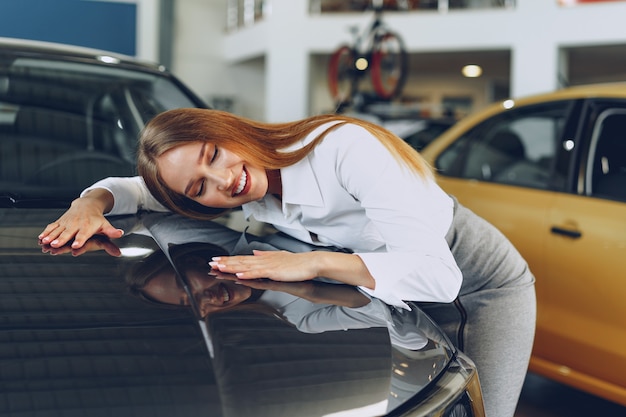 Belle jeune femme touchant sa nouvelle voiture avec plaisir et joie