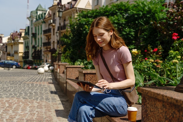 Belle jeune femme touriste avec café à emporter dans le centre-ville à l'aide de tablet pc.