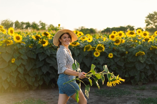 Belle jeune femme avec des tournesols appréciant la nature et riant sur le champ de tournesol d'été