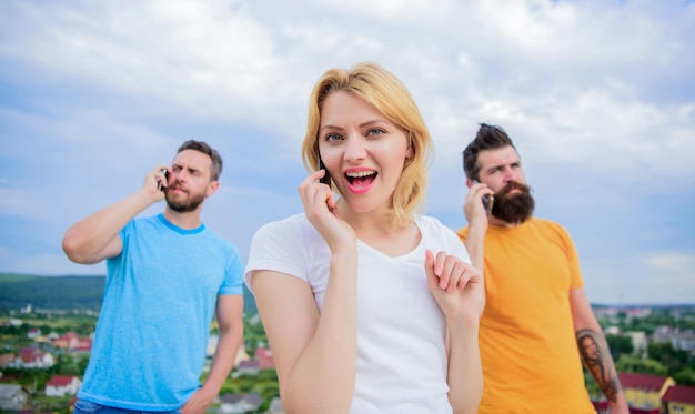 Belle jeune femme en train de parler au téléphone portable et souriante près d'amis debout en train de discuter dans le