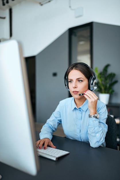 Belle jeune femme travaillant avec casque et ordinateur de bureau moderne.