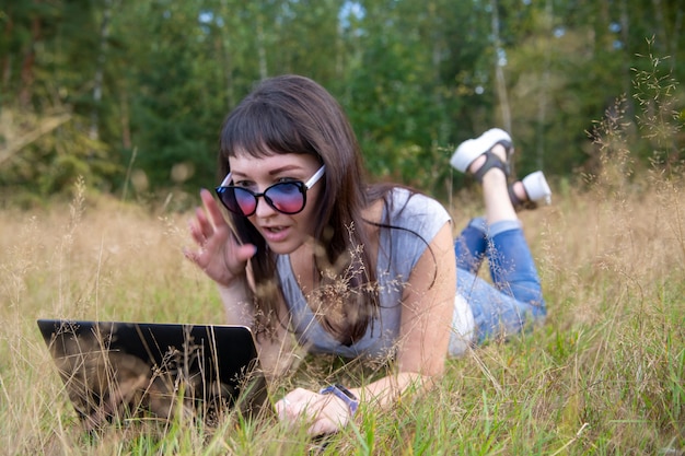 Belle jeune femme travaillant émotionnellement sur un ordinateur portable sur une pelouse ensoleillée par une chaude journée d'été heureuse