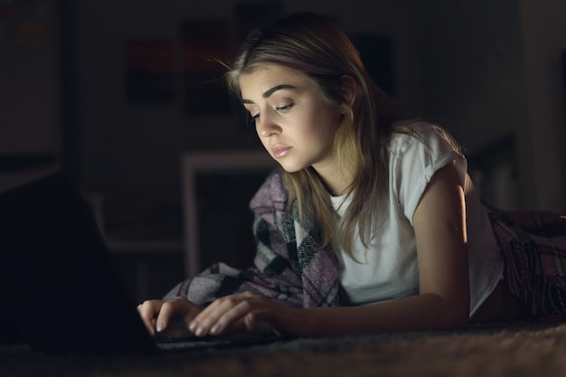 Belle jeune femme travaille la nuit à la maison pour un ordinateur portable