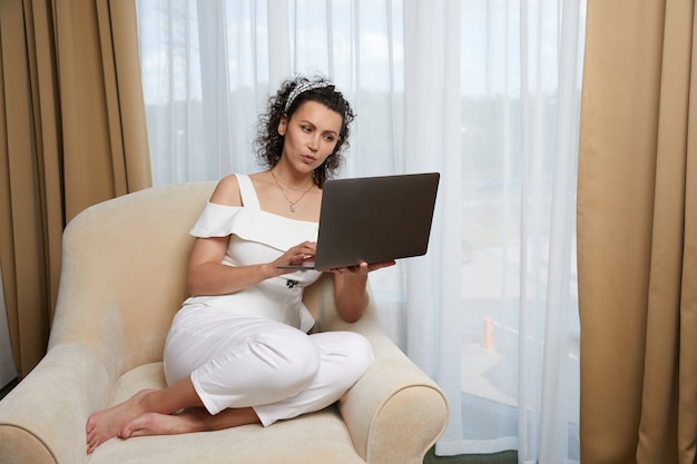 Belle jeune femme utilisant un ordinateur portable assis dans un fauteuil concept de femme d'affaires détendue à l'hôtel