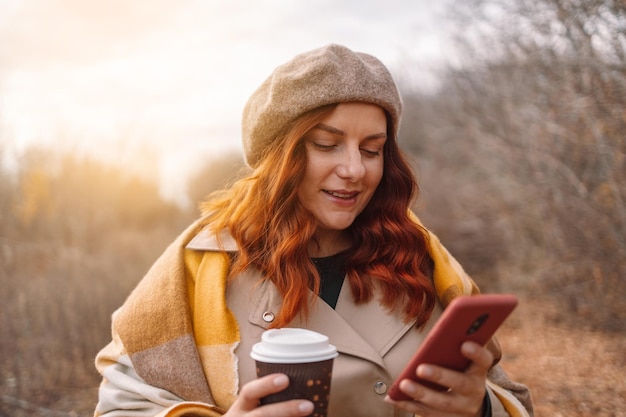 Belle jeune femme utilisant un smartphone et buvant du café à emporter au parc de la ville