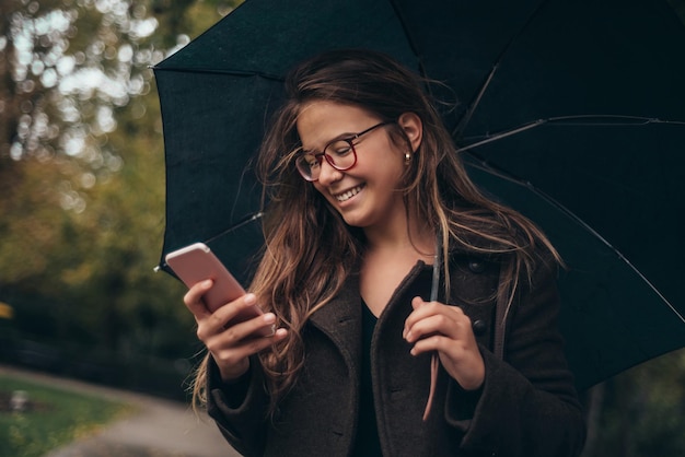 Belle jeune femme utilisant un smartphone et tenant un parapluie