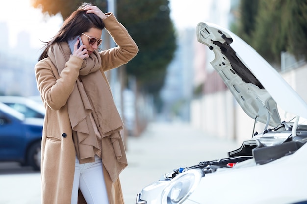 Belle jeune femme en utilisant son téléphone portable appelle à l&#39;aide pour la voiture.