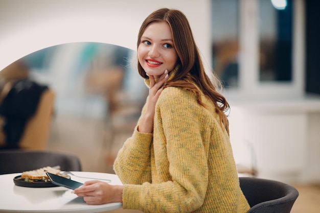 Belle jeune femme utilisant une tablette numérique à une table de café avec une tasse de café