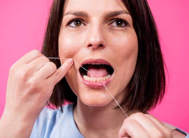 Belle jeune femme utilise du fil dentaire sur fond rose