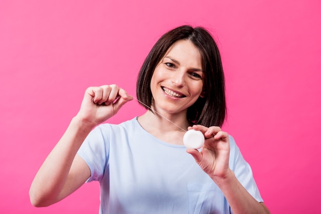 Belle jeune femme utilise du fil dentaire sur fond rose