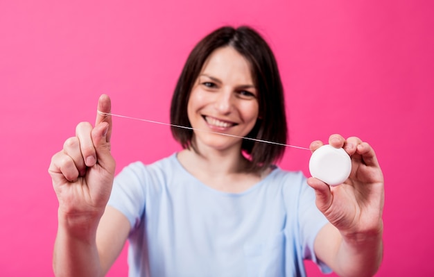 Belle jeune femme utilise du fil dentaire sur fond rose