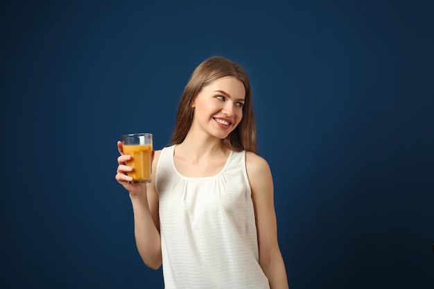 Belle jeune femme avec un verre de jus de fruits frais sur fond bleu foncé