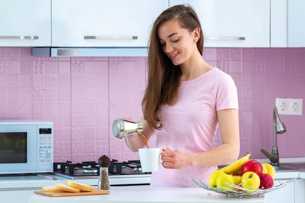 Belle jeune femme versant un café turc savoureux chaud de Cezve pour le petit déjeuner à la cuisine tôt le matin.
