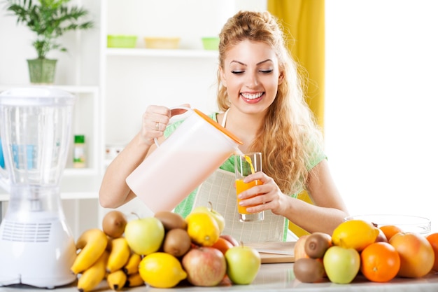 Belle jeune femme versant du jus d'orange au verre dans la cuisine.