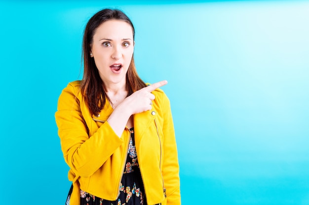 Belle jeune femme en veste jaune pointant de côté montrant la surprise