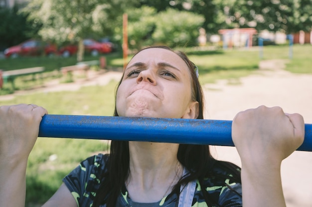 Une belle jeune femme en vêtements décontractés fait des exercices de traction sur la barre horizontale fitness sport exerçant la formation et le concept de style de vie jeune femme faisant des tractions sur la barre horizontale à l'extérieur